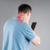 Man with neck pain from using smartphone, text neck and bad posture concept on gray background
