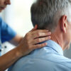 Doctor performs neck adjustment on patient. Hands gently manipulate back of head. Senior man receives physical therapy for pain relief. Health care provider helps improve, posture and mobility.