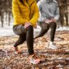 Close up of shape fitness girl in sportswear doing leg stretching with her personal trainer in the forest in the sunny winter morning.