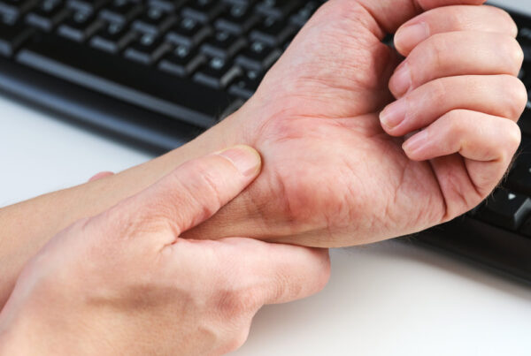 A man massaging his painful wrist against a background of a computer keyboard, illustrating the discomfort of carpal tunnel syndrome. Close up.