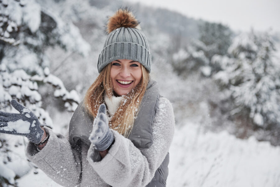 Conception of winter holidays. Cheerful girl in warm clothes playing with snow outdoors near the beautiful forest