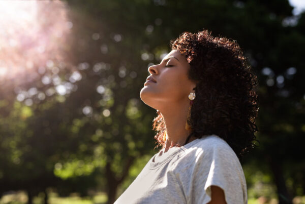 Young woman standing with her eyes closed and head raised to the sky in a park on a sunny summer afternoon