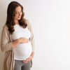 Portrait shot of young beautiful woman on third trimester of pregnancy. Close up of pregnant female with arms on her round belly. Expecting a child concept. Background, copy space.