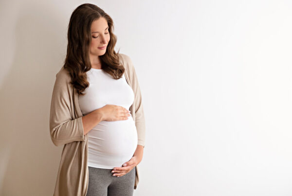 Portrait shot of young beautiful woman on third trimester of pregnancy. Close up of pregnant female with arms on her round belly. Expecting a child concept. Background, copy space.