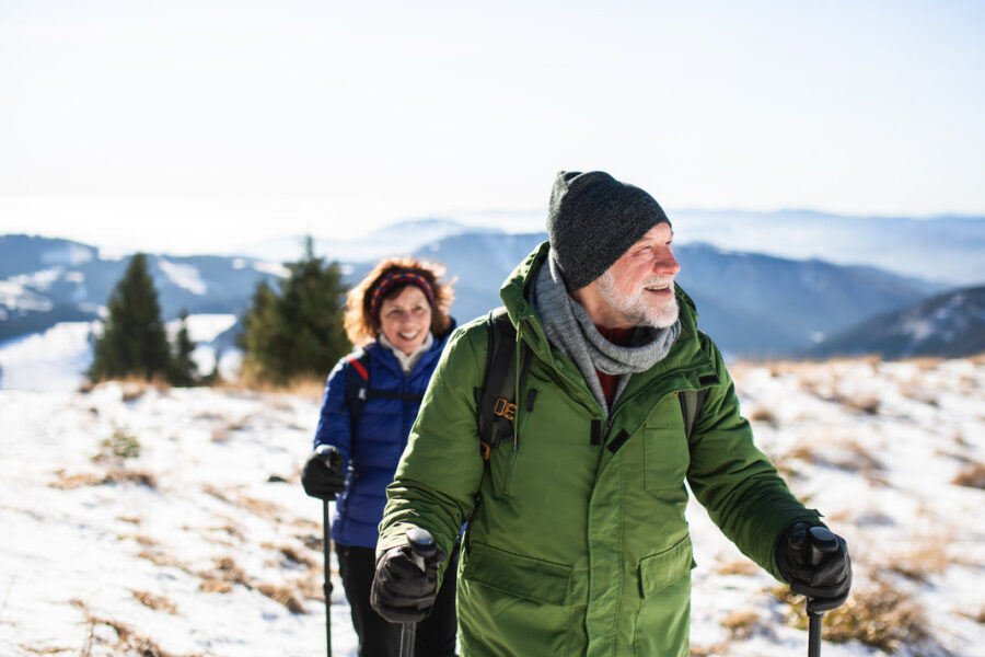Senior couple with nordic walking poles hiking in snow-covered winter nature, healthy lifestyle concept.