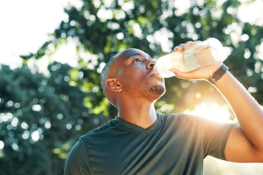 Fitness, black man and drinking water outdoor for health, wellness and exercise recovery.