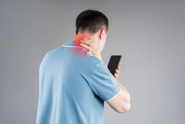 Man with neck pain from using smartphone, text neck and bad posture concept on gray background