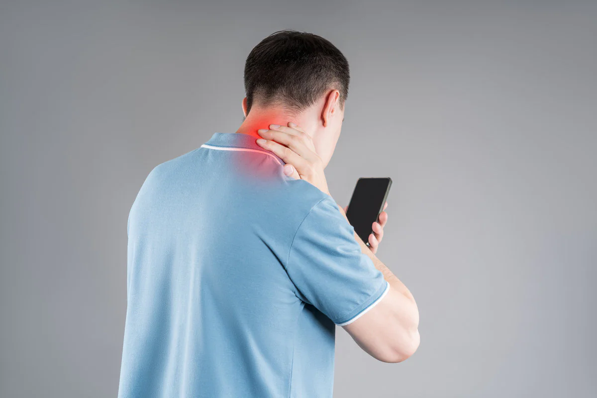 Man with neck pain from using smartphone, text neck and bad posture concept on gray background