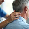 Doctor performs neck adjustment on patient. Hands gently manipulate back of head. Senior man receives physical therapy for pain relief. Health care provider helps improve, posture and mobility.