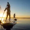 Men, friends sail on a SUP boards in a rays of rising sun