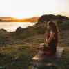 Woman doing yoga alone at sunrise with mountain and ocean view. Harmony with nature. Self-analysis and soul-searching