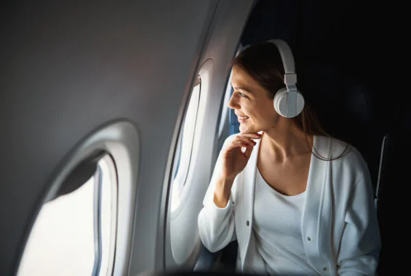 Positive young woman in headphones smiling while looking outside of the airplane. Website banner