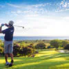 Man hitting golf ball down hill towards ocean and horizon