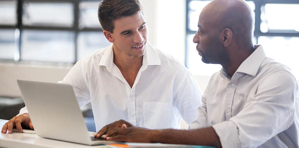 Two men are discussing something on a laptop.