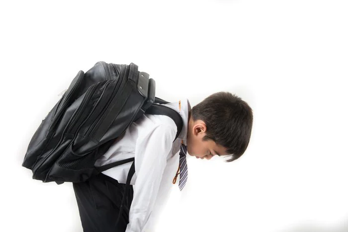 Young boy carrying a heavy school backpack on his back