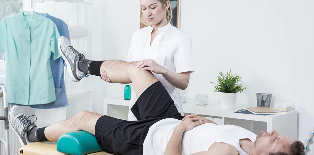 A female chiropractor massages a man's knee.